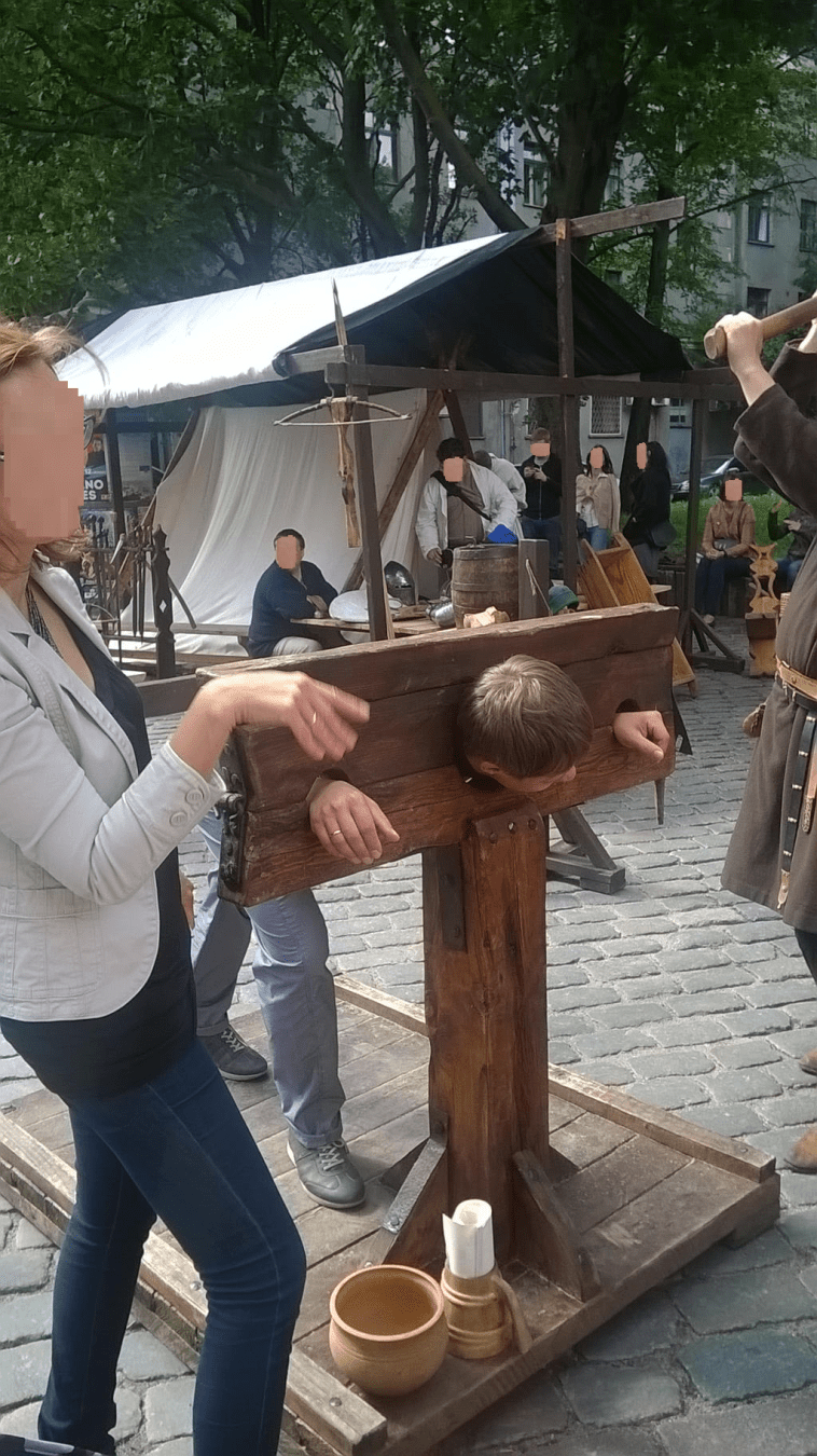 A man is in the stocks, with his partner explaining why he has been sentenced