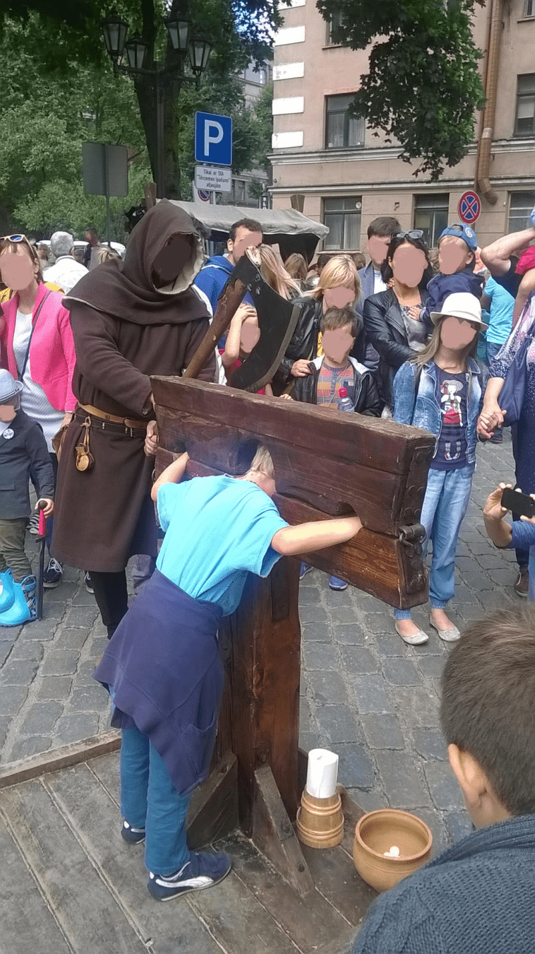 A young boy is in the stocks, the Executioner readying his axe