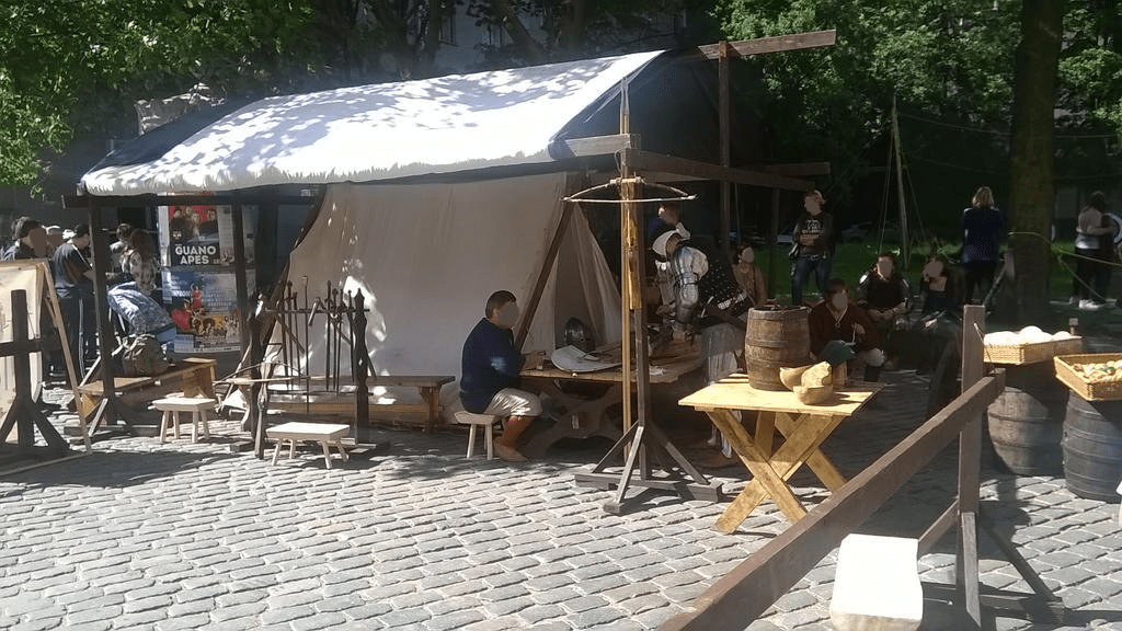 Tent of the knights, with some having a lunch break, with weapons and tools in the area