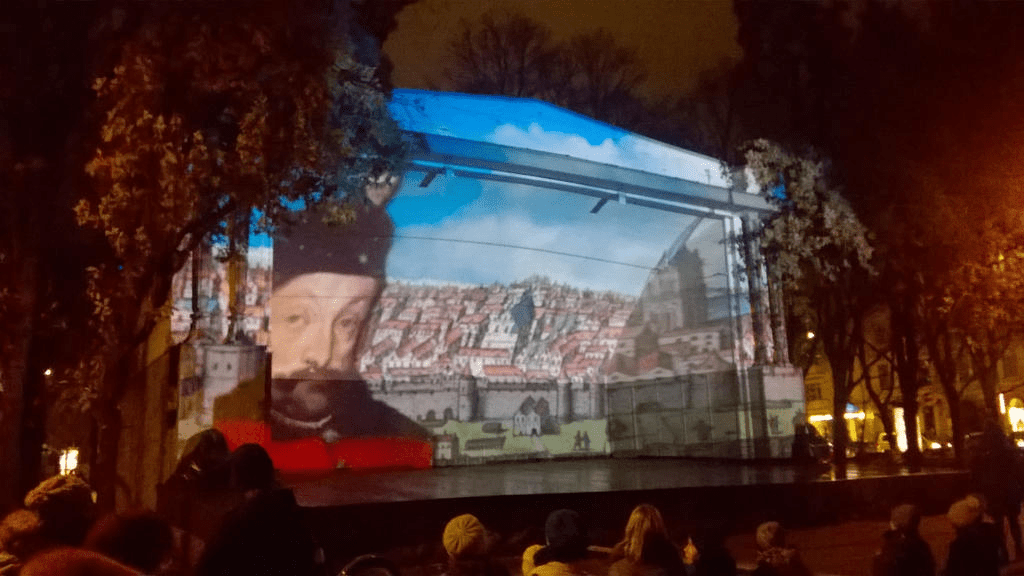 A man in red and black slides in front of the now brightened painting of Riga from the middle ages