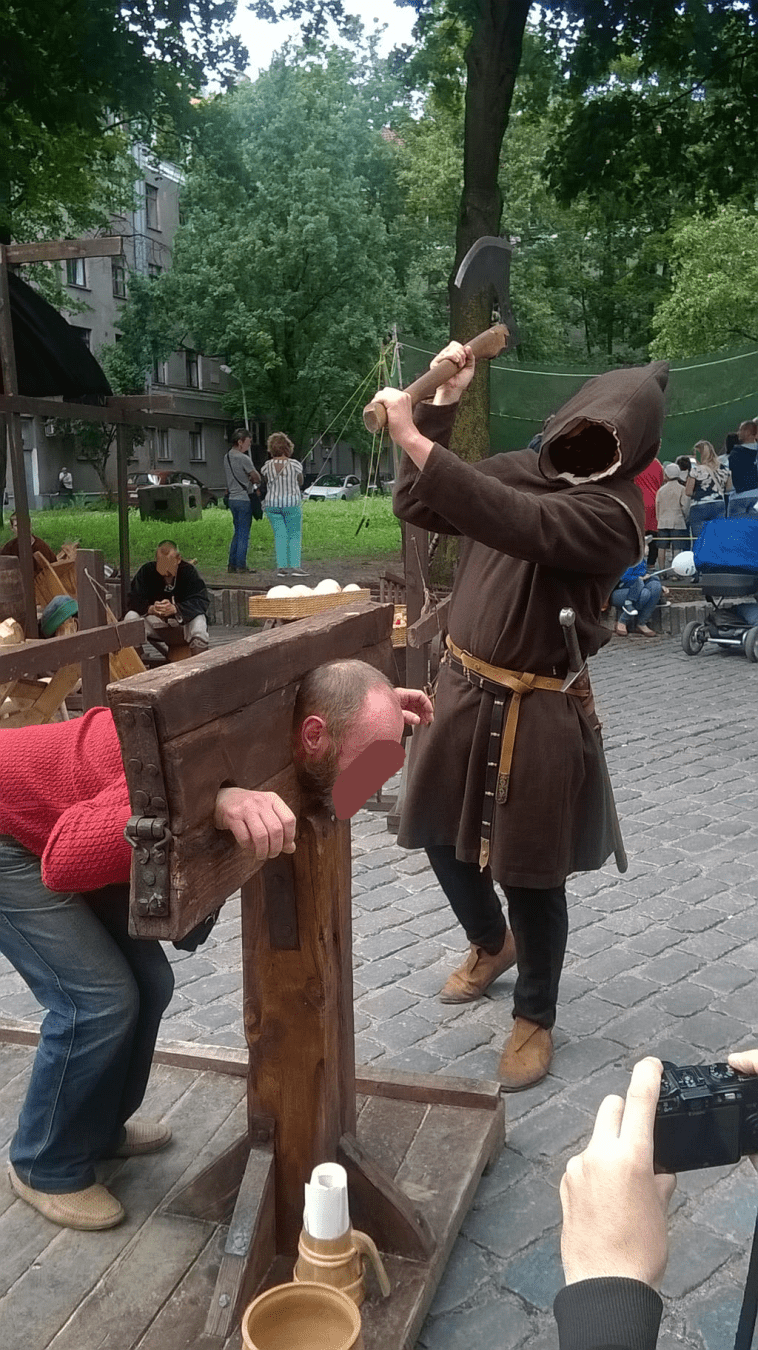 An older man is in the stocks and the axe is raised up high
