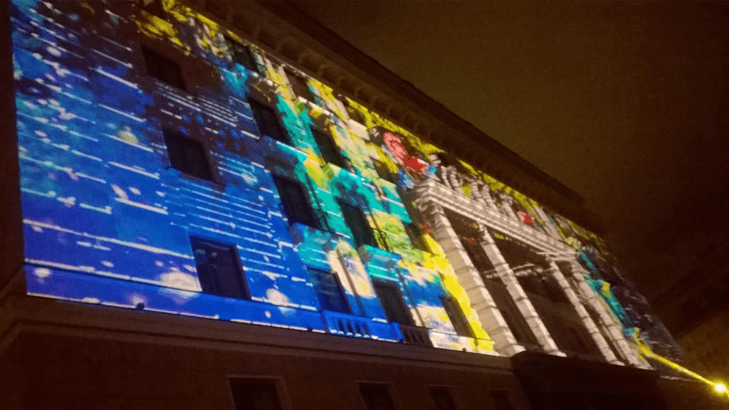 Hotel facade, lit up with blue flames turning into yellow flowers