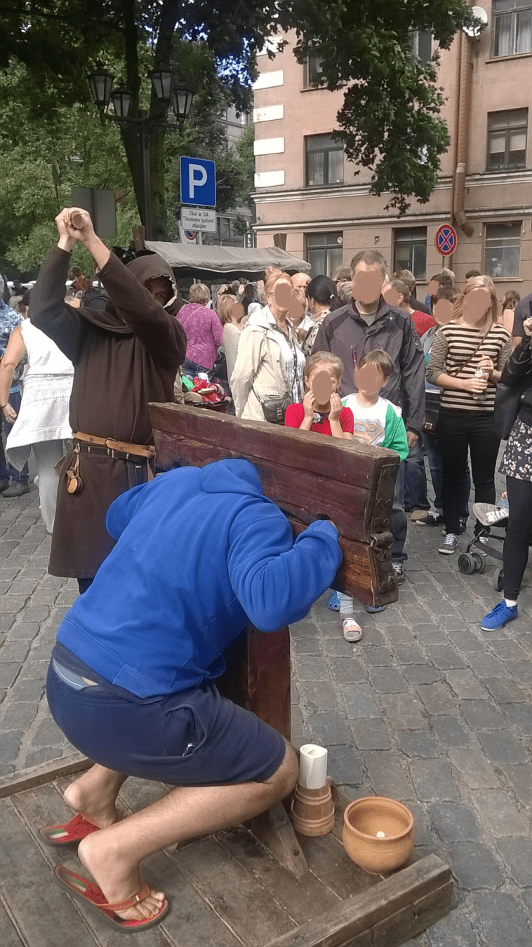 A tall man crouching to fit into the stocks, the Executioner raised his axe up high