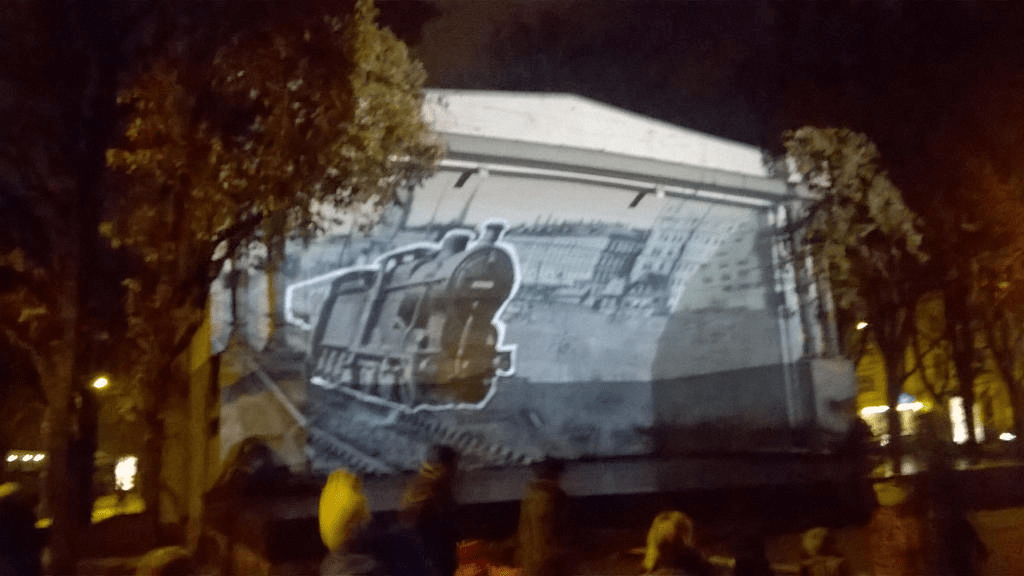 Cutout of a train, travelling by a grey photo of Riga