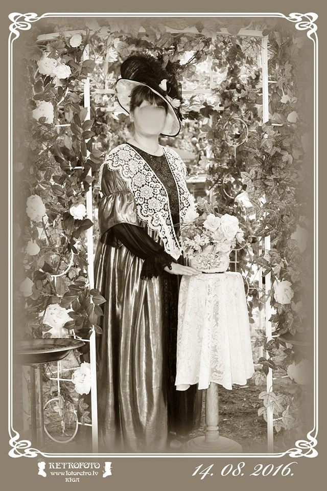 Retro style sepia toned photo of a young woman in a fancy dress and hat, standing by a small table and flowers