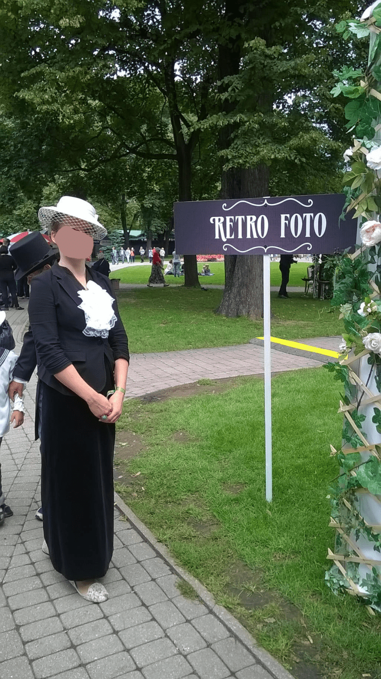 Lady in a retro outfit, standing by the retro photo booth sign by the white tent
