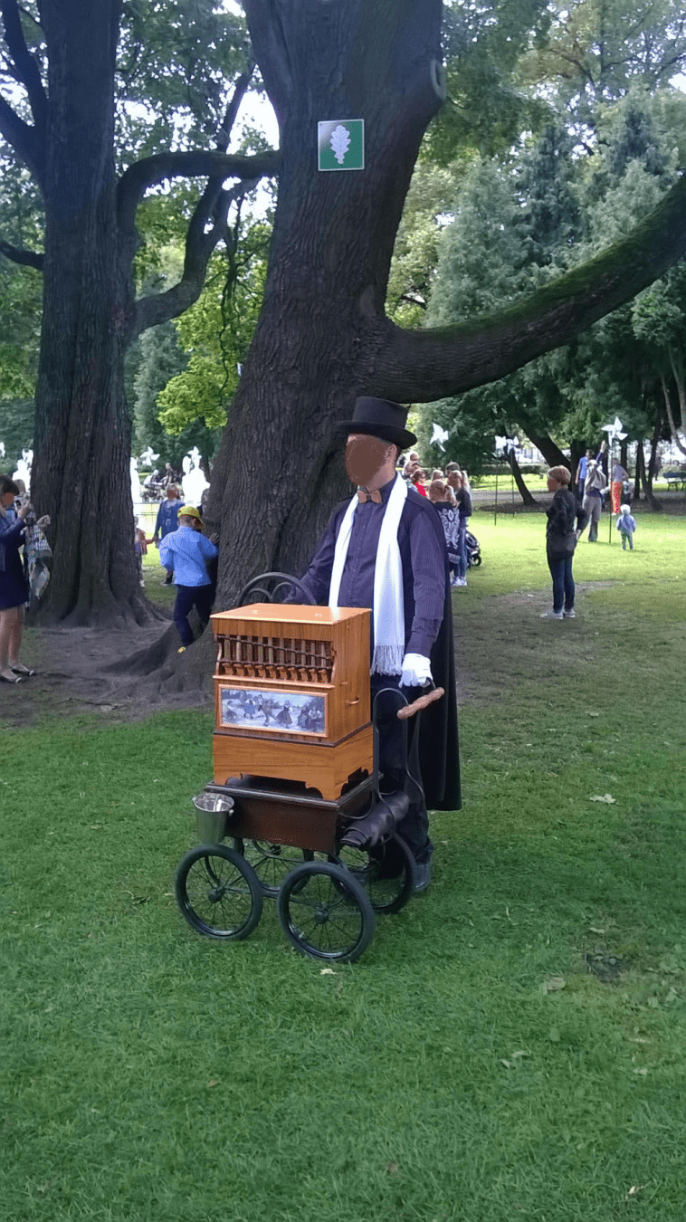A musician dressed in old timey outfit, playing his Organ Grinder for people to enjoy