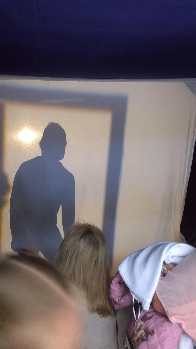 Inside of the tent, full of people, with the shadow of a person trying to remain inside of a moving shadow frame