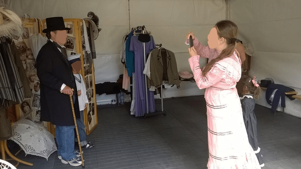 Fair attendants, wearing retro outfits, taking photos of a gentleman and kiddo in outfits having a small photoshoot in the tent