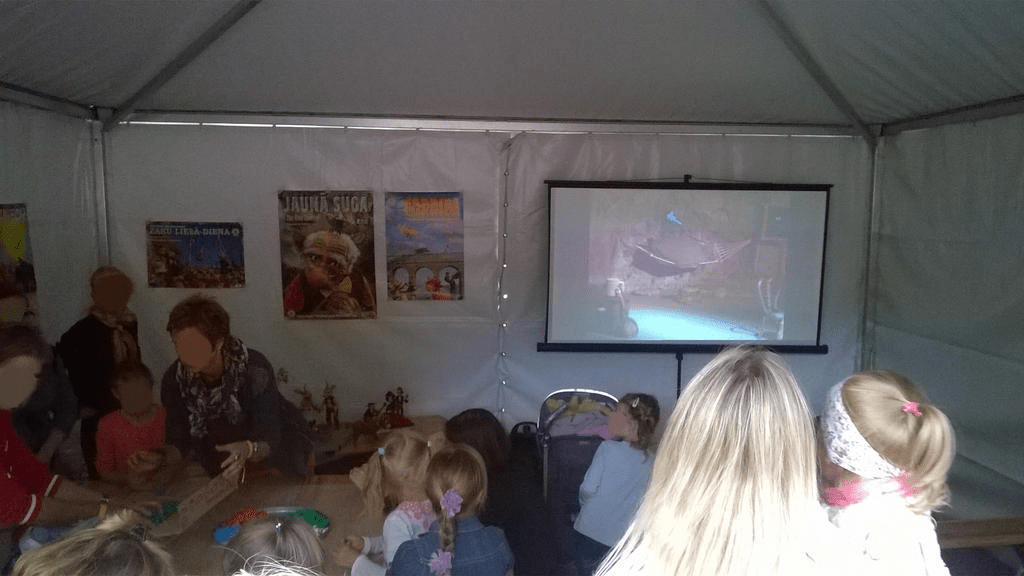 Inside look of the tent, with a screen having a movie projected on the screen and kid either watching or working on their projects