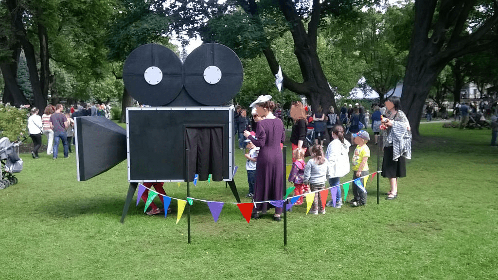 The camera and the line to it from the side, fair workers keeping order as kids took their turns