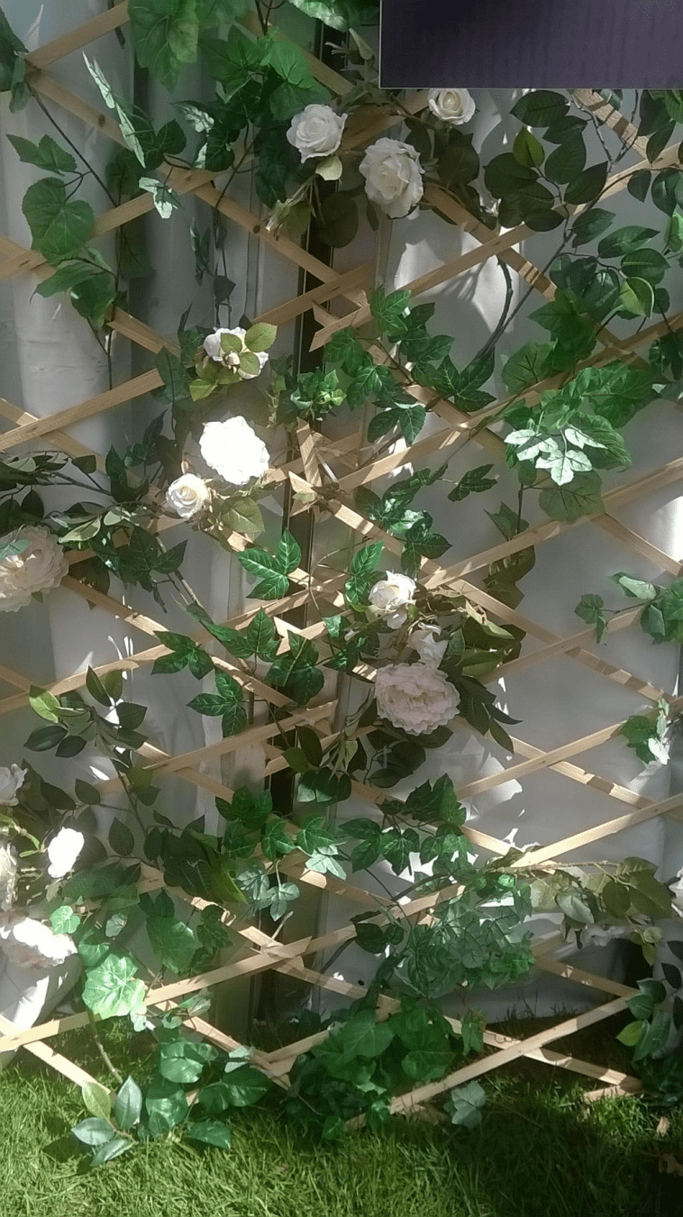 Fake white roses and leaves on a decorative stand leaned by the white tent