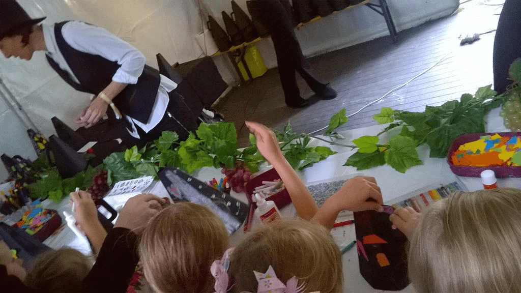 Photo of a group of kiddos, making paper megaphones, with an attendant explaining the process
