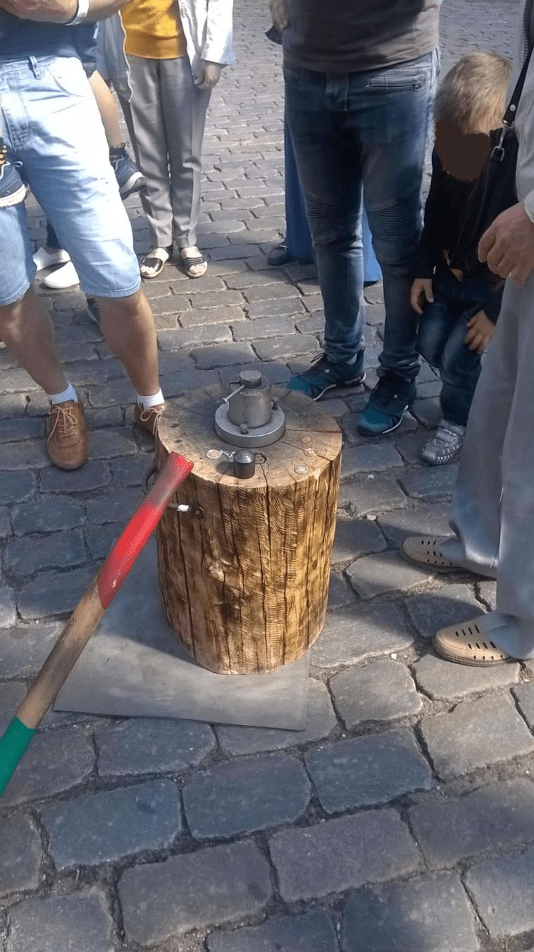 Photo of a coin being smashed with a heavy metal hammer flat on a wooden stump