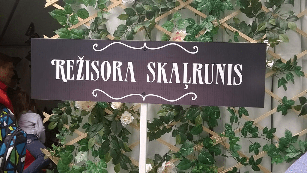 Black and white sign that in Latvian says "Directors Megaphone", in front of a white tent