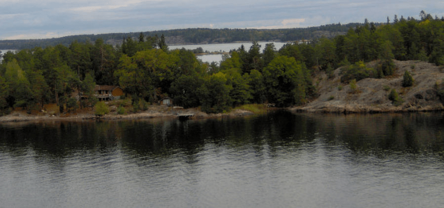 Long forested stony island with a two-story house on it and a dock nearby