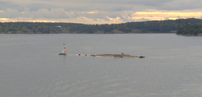 Small sandy island in the bay, with a structure near it, to warm of its presence