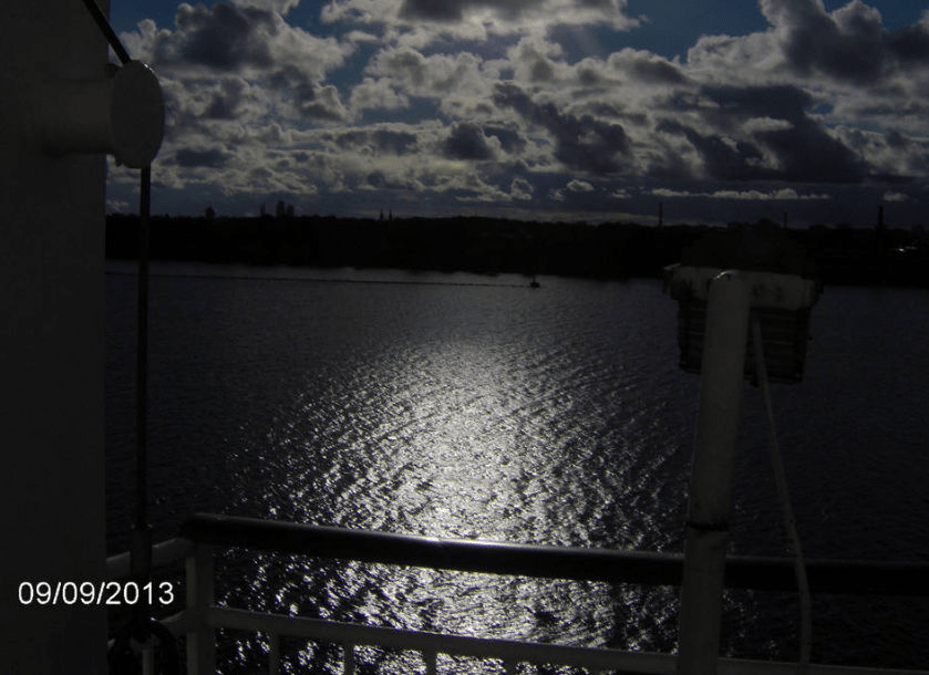 Photo from the cruise ship Tallink, looking over Daugava, very dark due to the clouds blotting out the sun, though a white spot is visible in the water