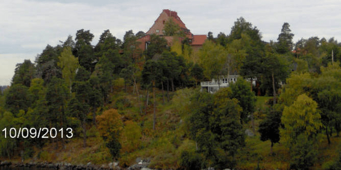Homes on a tall forested island, one small and white and one big and red