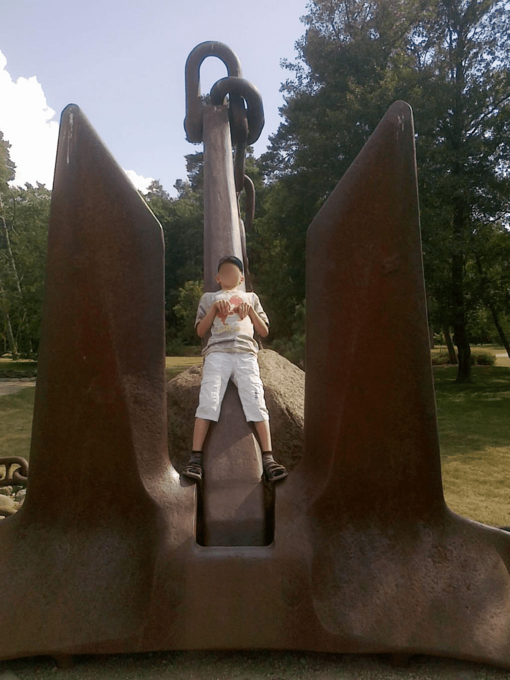 Young boy laying on his back on a huge anchor, hands bent like a T-Rexs