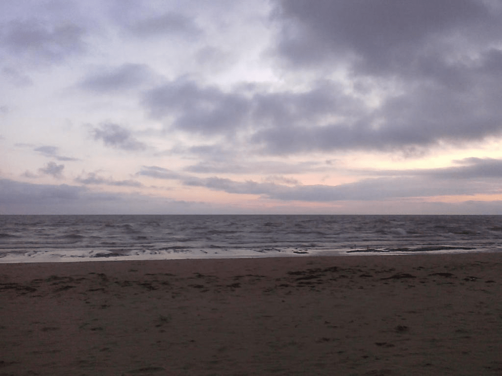 Beach, water is calm, the sky is darkening with clouds and the setting sun