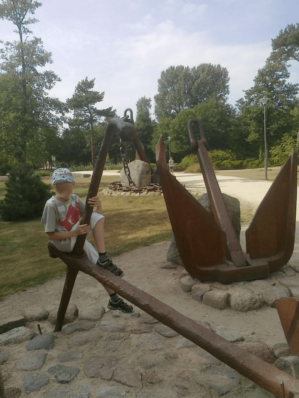 Young boy sitting atop of a thin big anchor, with more visible in the background
