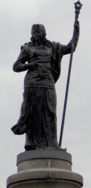 Statue of a woman with a staff in hand, standing on top of a bridges pillar