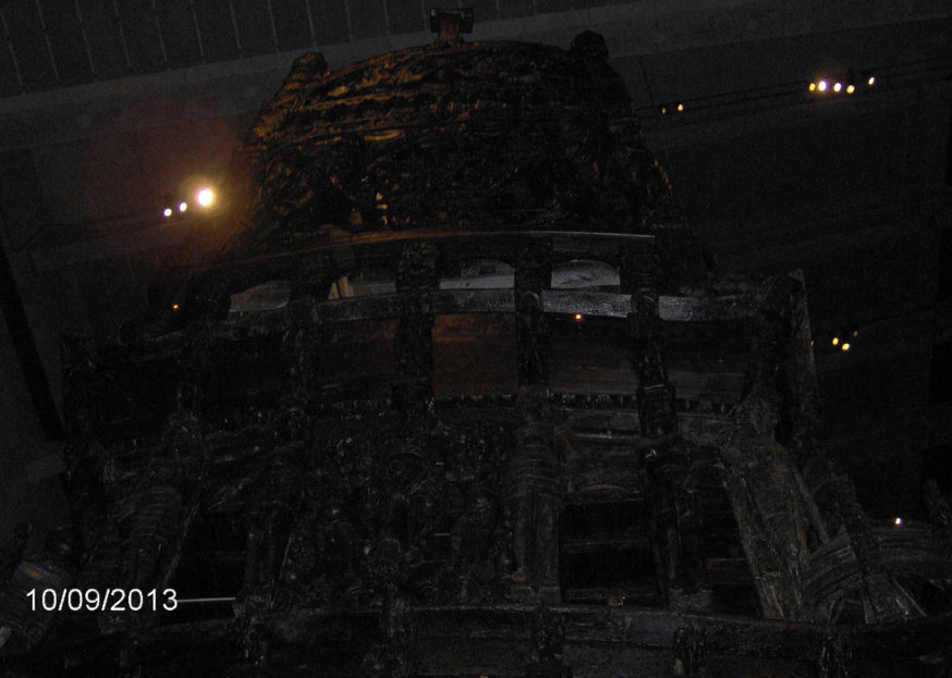 Upwards angled photo of the back of the Vasa, the dark wood hard to see against the dark ceiling