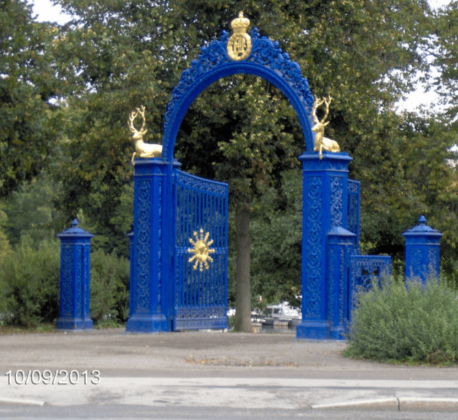 Blue gates with golden deers and symbols on it, in front of a park area