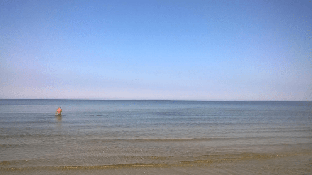 Shot of the Gulf of Riga from the Majori beach, the waves calm and sky clear. Someone is in the water in the distance