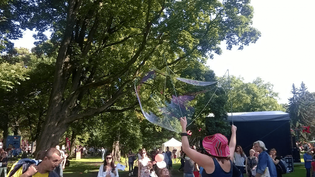 A fair workers is using fishing rods and soap soaked rope to make a BIG bubble for the crowd to enjoy
