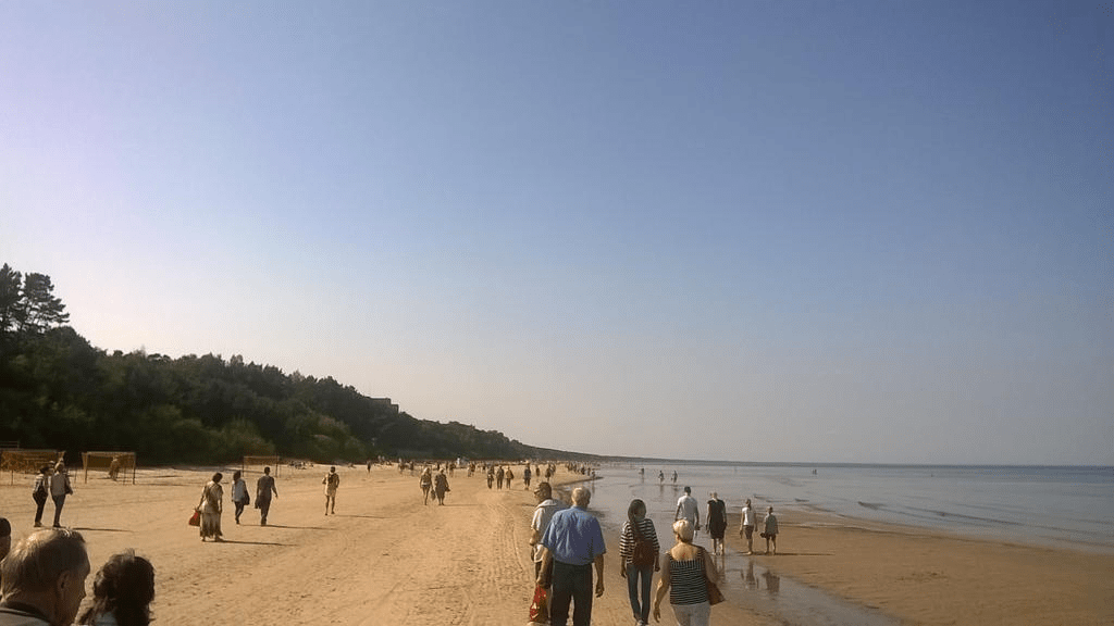Photo of the beach side, with people in various stages of clothing walking by the water