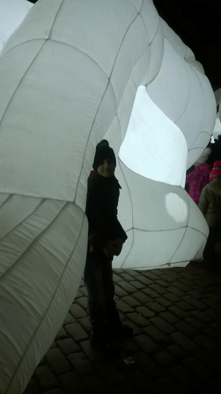 A young boy in winter clothes is leaning against the ear of the big balloon bunny