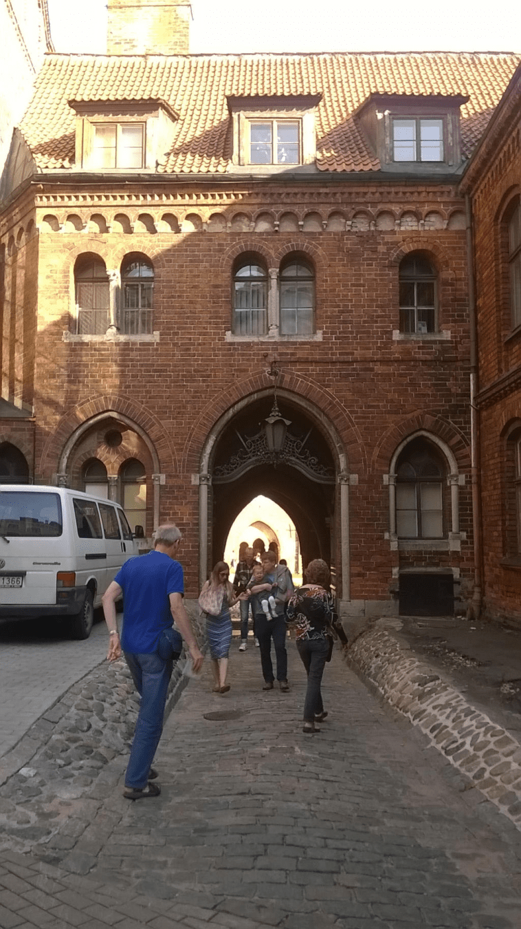 Photo to the entrance of the Doma Cathedral inner square, with the gates open, with a bunch of people going in and coming out.