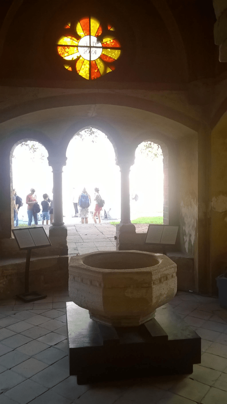 A stone fountain-type thing in the middle of a small room to the door to the courtyard of the cathedral