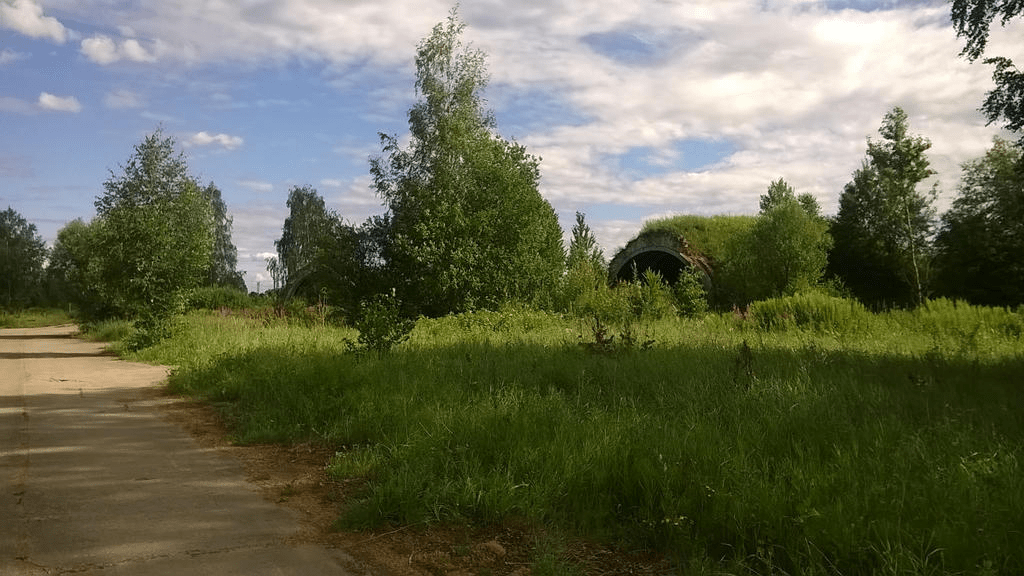 At least two grass covered hangers are visible in the lush grass to the right of the dusty road, hidden by the trees