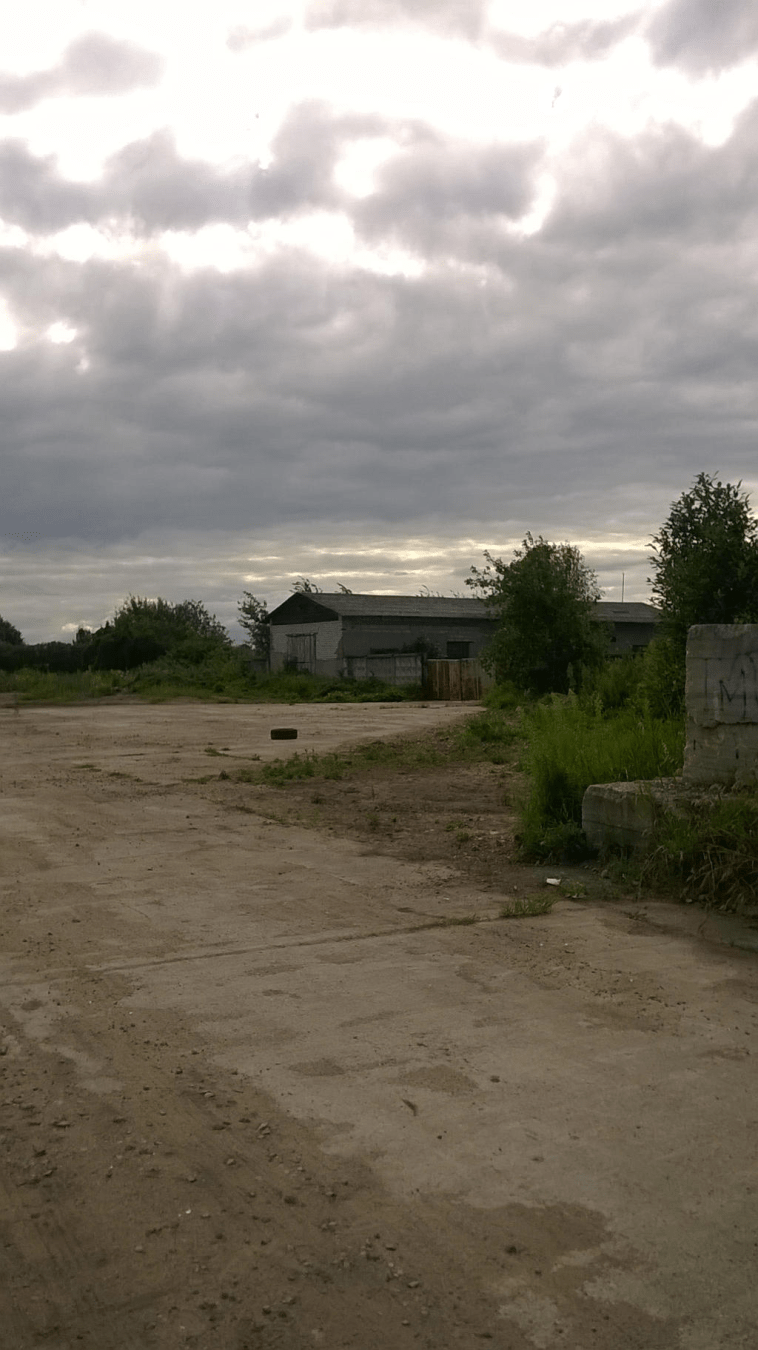 Old building behind stone gates, the sky overcoast and the road is dirt
