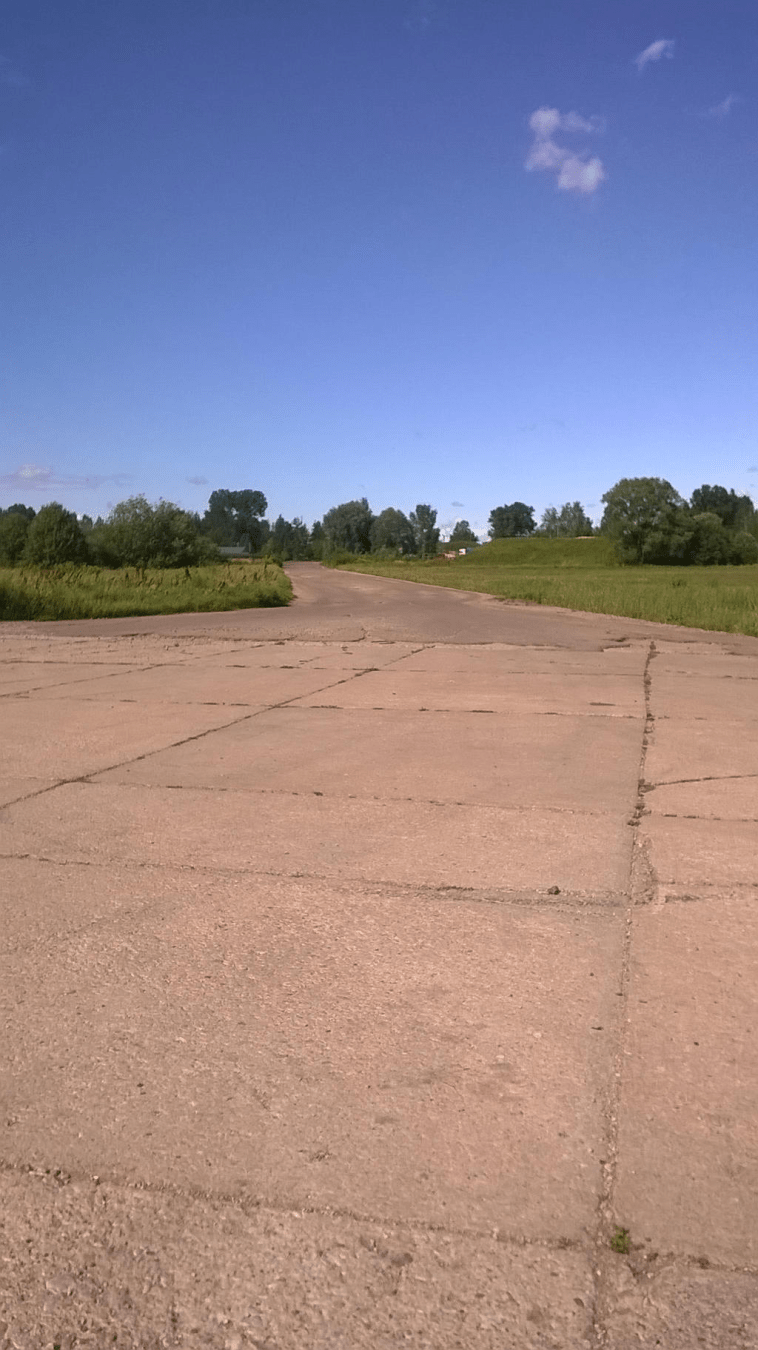 Old runway leading up to a newer road through lush grass and patches of trees