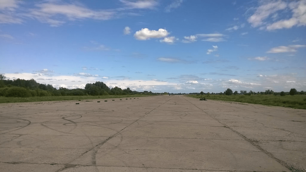 The old runway, with lush grass and patches of trees on the right and a forest-ish area on the left, with tires positioned and tiremarks on the ground