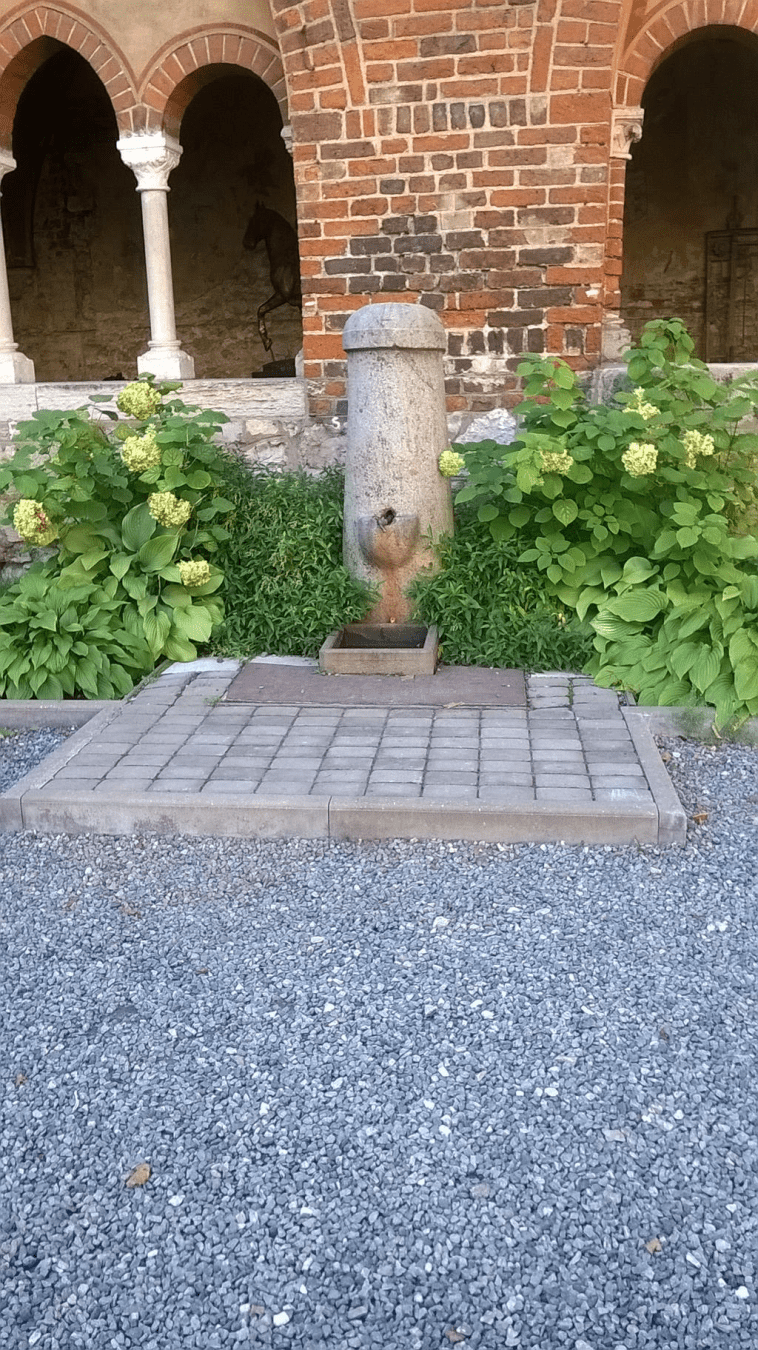 Small water fountain in the cathedral courtyard, with bushes around the sides