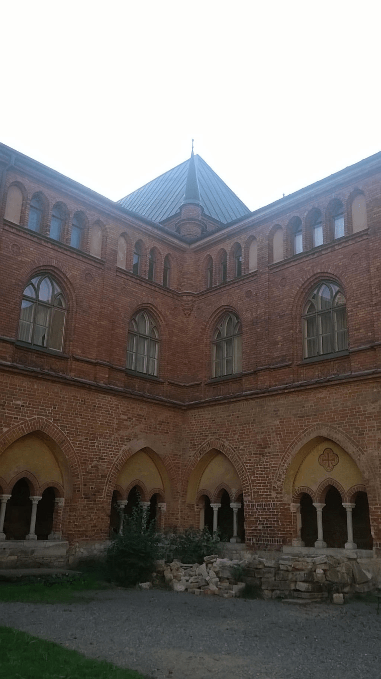 Corner of the Doma Cathedral courtyard, the corner with small bushes and stones in and around it, with a very brigth sky