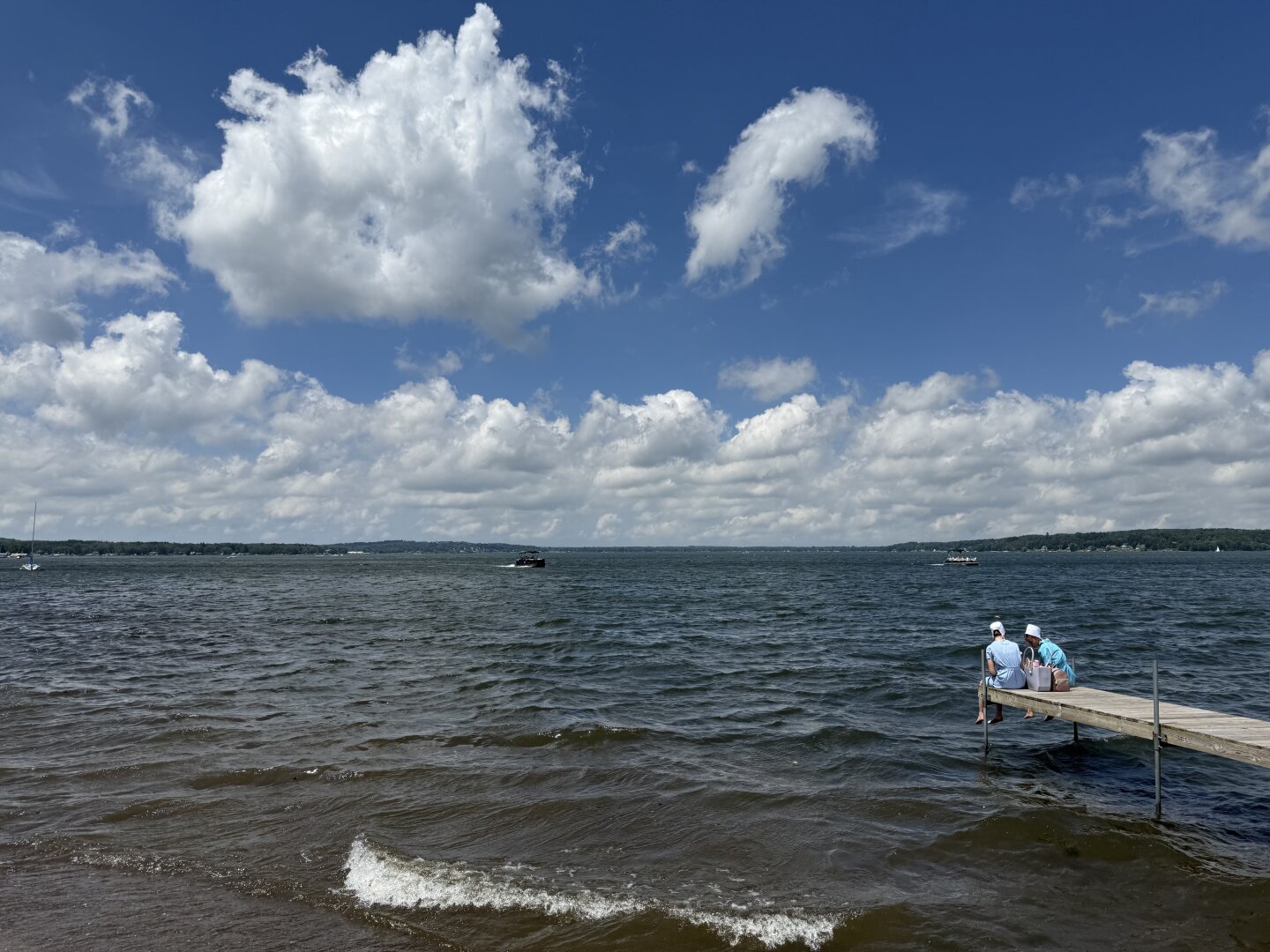 Two women sit on a pier next to a lake