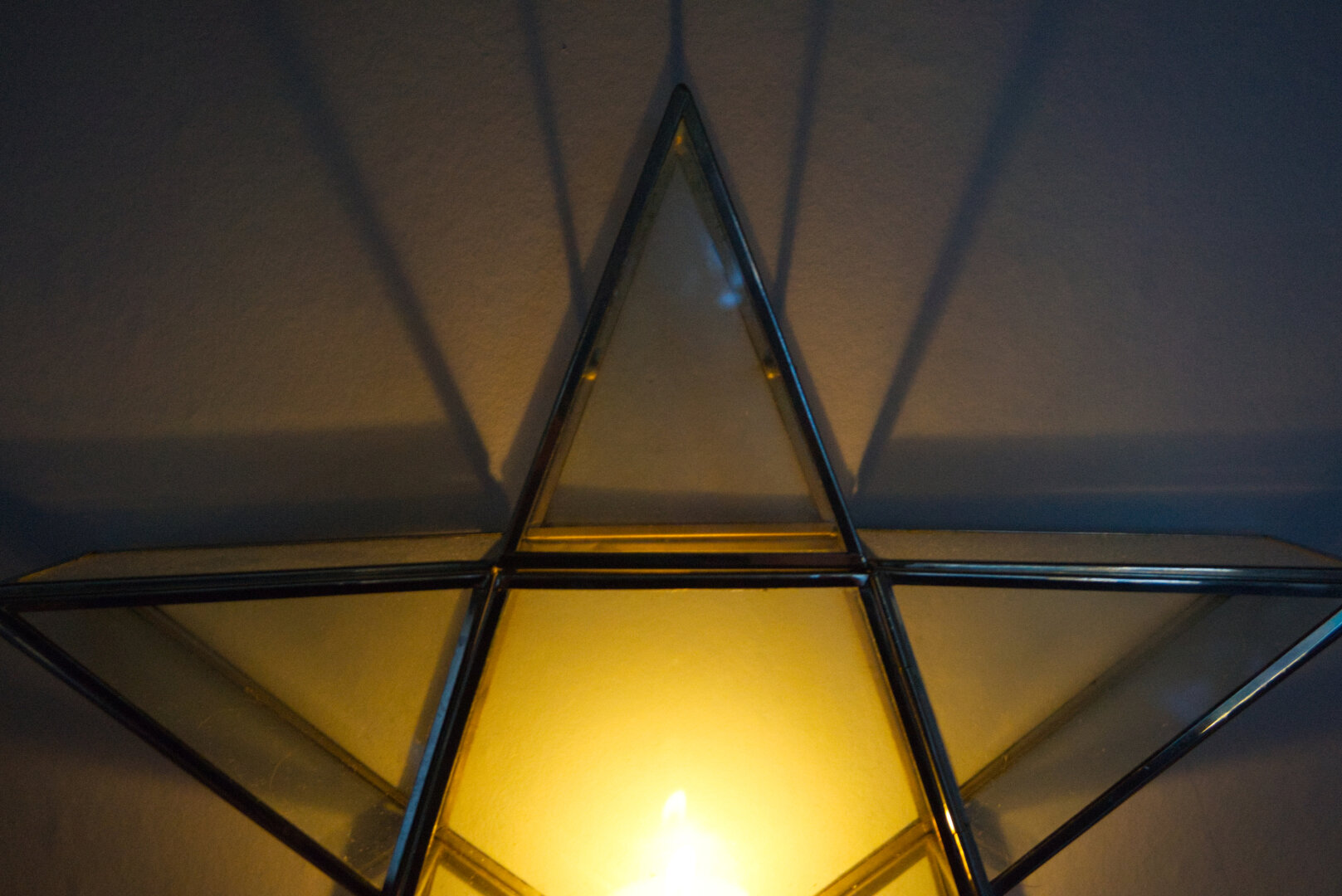 A candle in a star-shaped glass holder with silver outlines casting shadows on the wall behind.