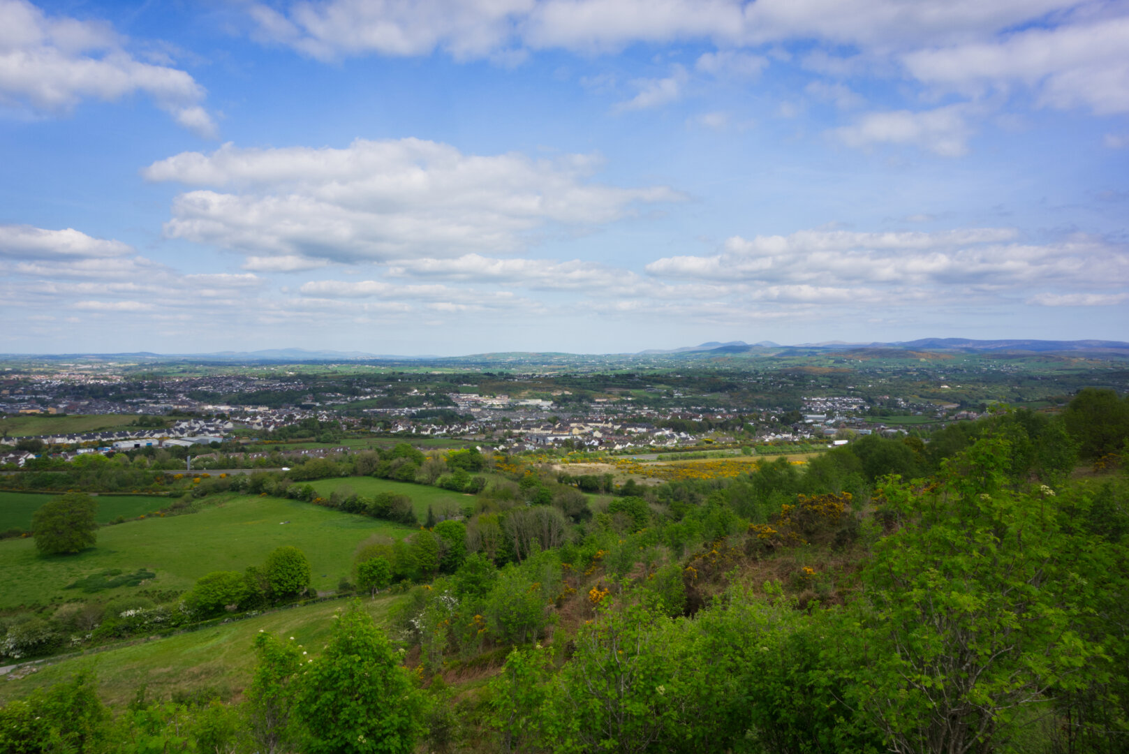 The view over Newry city and the surrounding landscape from above, with a vibrant blue sky and fluffy white clouds.