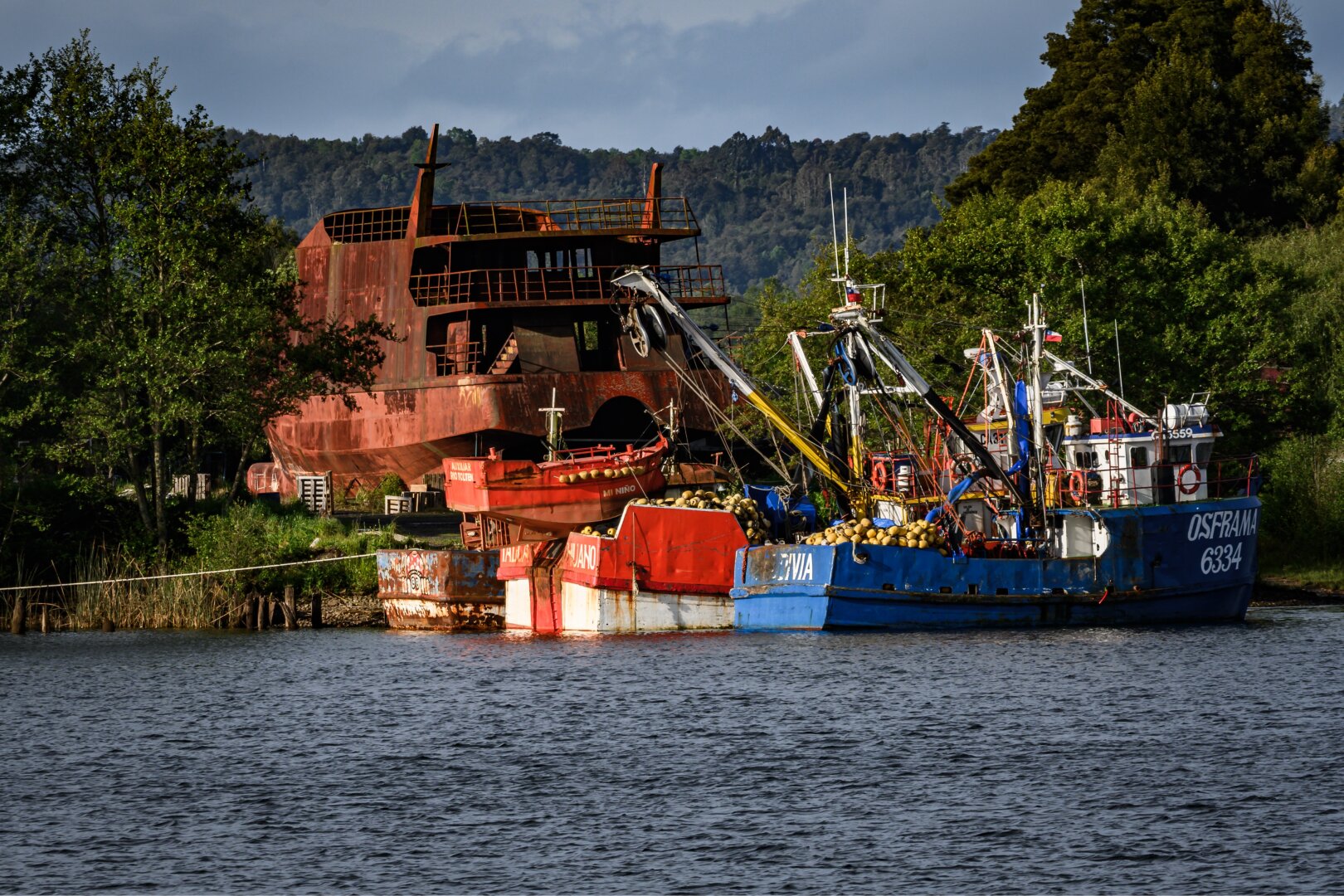Fishing boats anchored on the river near a rusted old ship