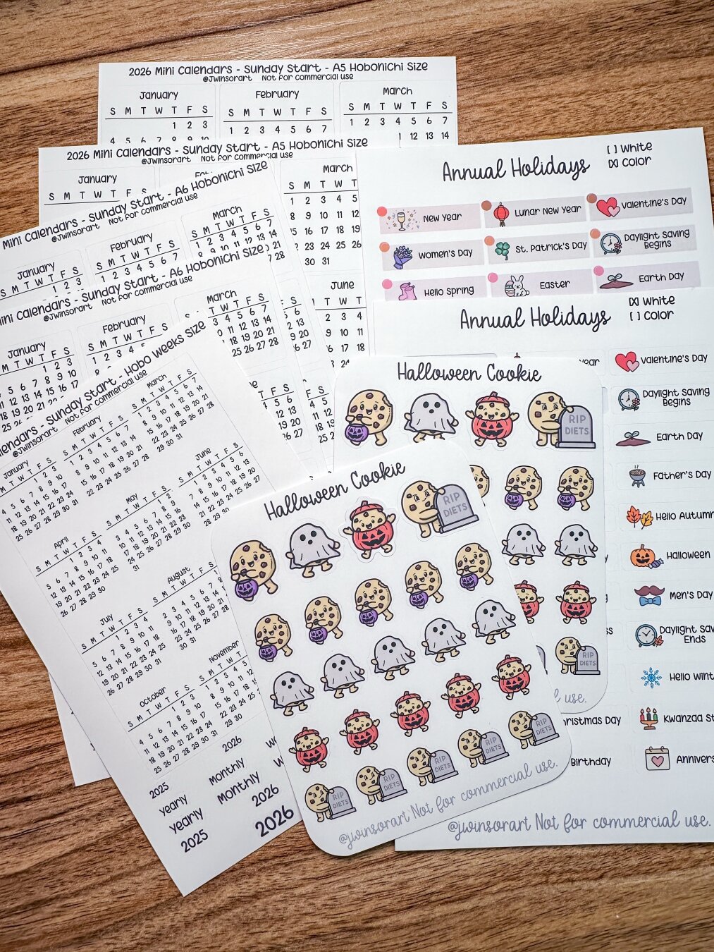 A flat lay of printed sheets, including mini calendars for 2026, holiday stickers, and themed cookie designs for Halloween, all displayed on a wooden surface. The design features colorful graphics and notes related to various annual holidays.