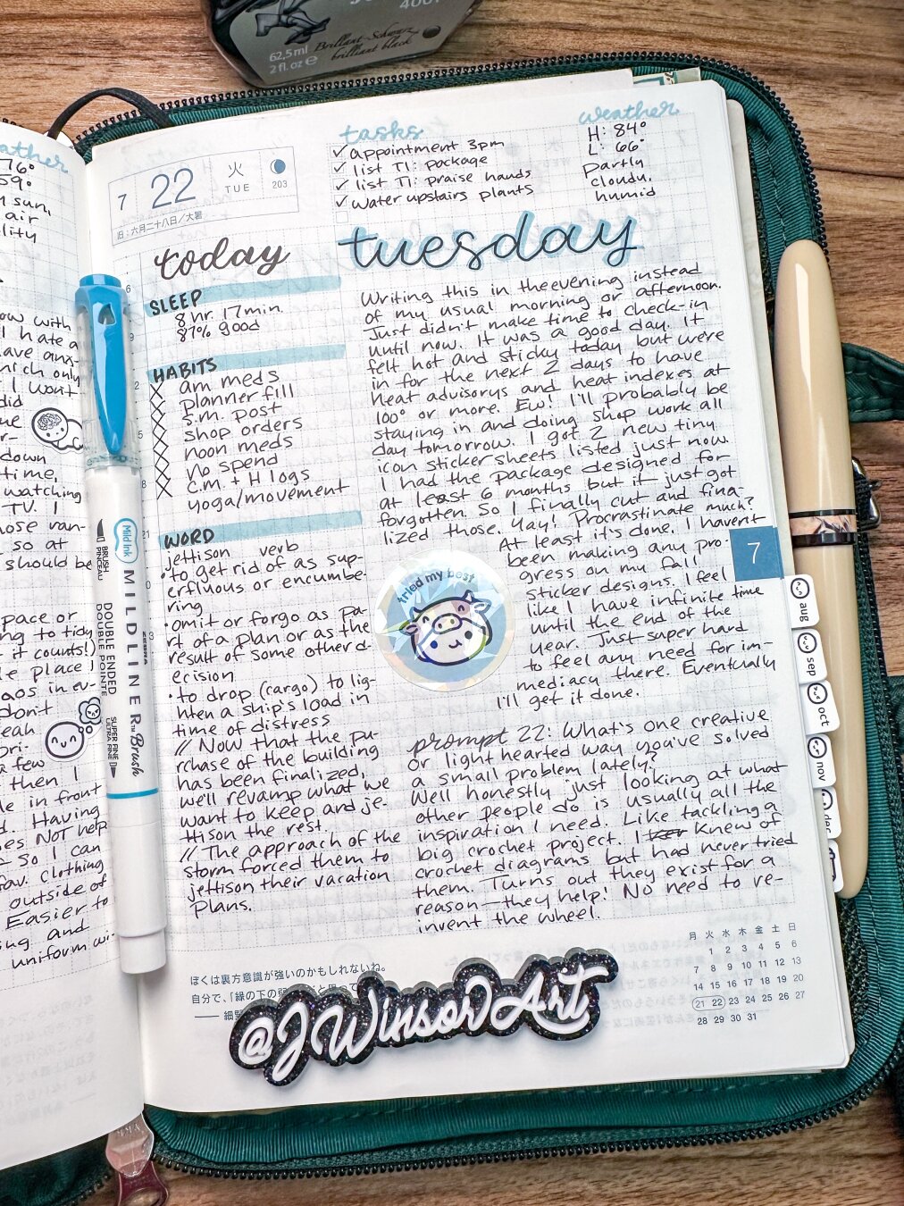 Hobonichi daily journaling page for July 22, 2025. Has light blue brush lettering and stickers by TheCoffeeMonsterzCo on the page. In a dark green POTR zip case.