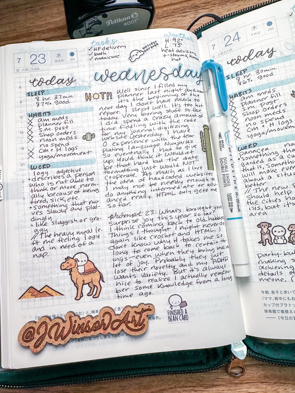 A journal page with handwritten notes, dated July 23 and 24, displays daily reflections, tasks, and sleep logs. There are illustrations, including a cartoon of a person riding a camel and decorative elements like mountains. A blue Zebra Mildliner marker lies in the middle of the pages and a Pelikan ink bottle sits at the top of the Hobonichi planner.