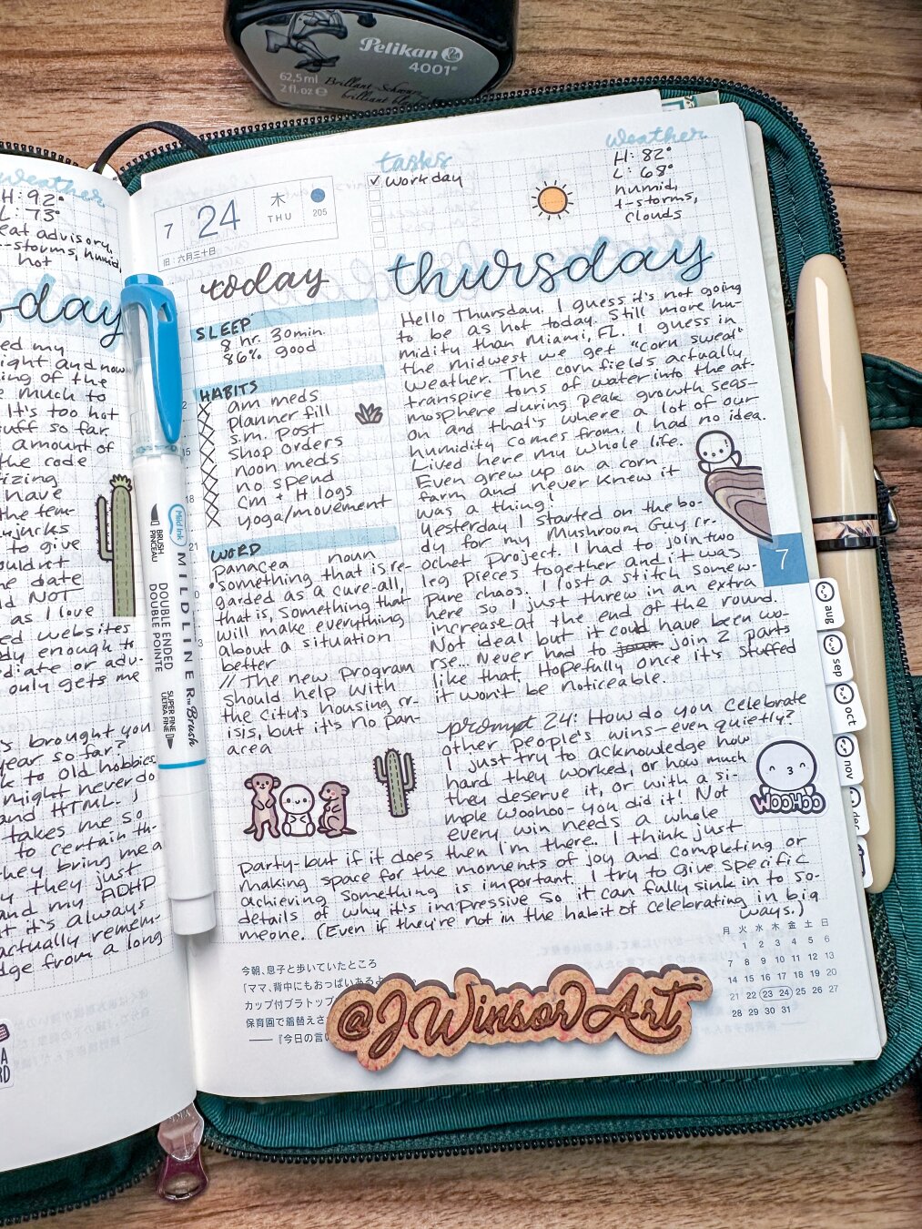 A journal page with handwritten notes, dated July 23 and 24, displays daily reflections, tasks, and sleep logs. There are illustrations, including a cartoon of a person riding a camel and decorative elements like mountains. A blue Zebra Mildliner marker lies in the middle of the pages and a Pelikan ink bottle sits at the top of the Hobonichi planner.