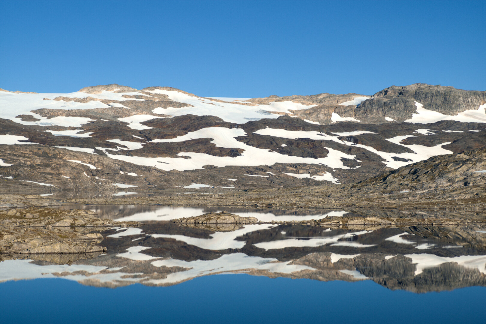scenic view over a perfectly still mountain lake, mirroring blue sky and a glacier behind